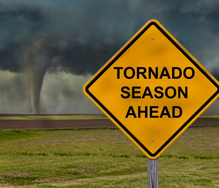 A tornado forms on a plain of grass with a sign that reads "Tornado Season Ahead"