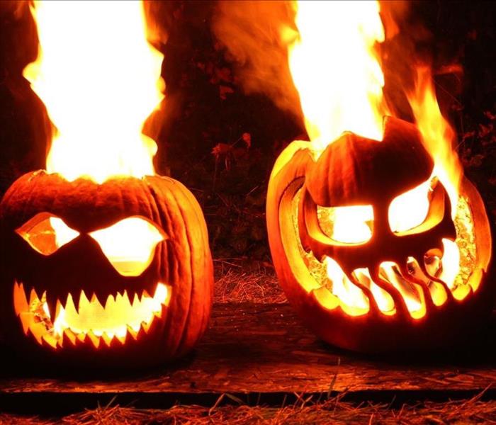 Two jack-o-lanterns that are on fire while it is dark outside.