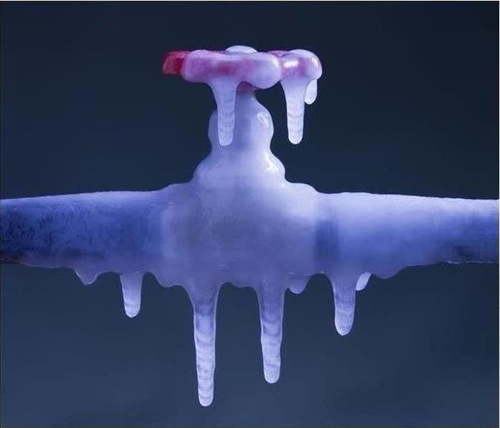 A water valve on a pipe is covered in ice and frozen in place.
